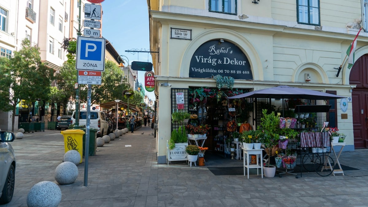 A flower shop on a street corner in Budapest with potted plants and signage